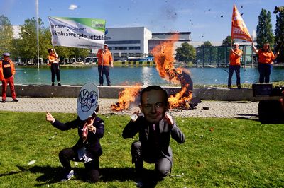 Wissing und die Autoindustrie hocken im Graß und hinter ihnen brennen die Reste der 1,5° lichterloh