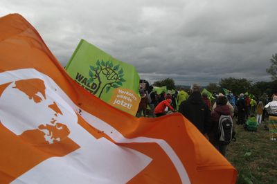 Im Vordergrund eine wehende Attac-Fahne, im Hintergrund Kundgebung