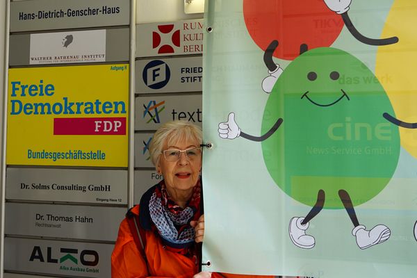 Eine Aktivistin hält das Banner, neben ihrem Kopf ist das Klingelschild der FDP zu sehen