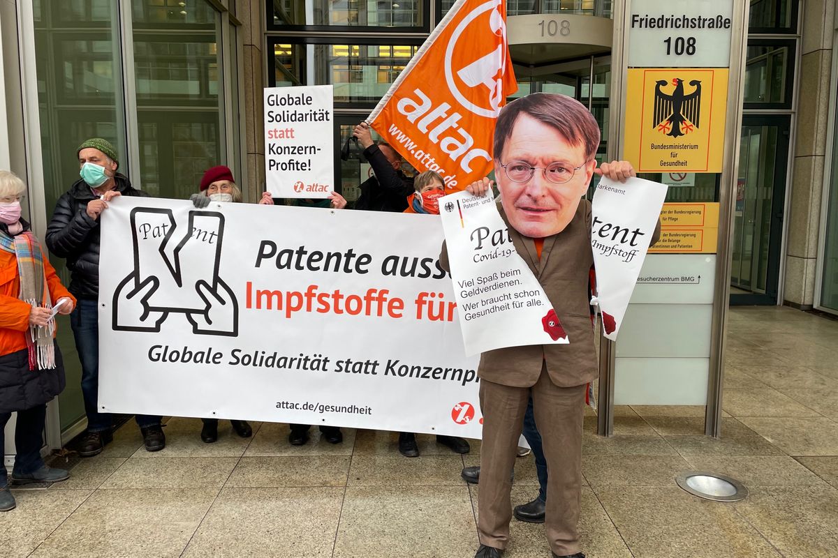 Ein als Karl Lauterbach verkleideter Aktivist zerreißt vor dem Bundesgesundheitsministerium ein übergroßes Patent. Im Hintergrund ist ein Transparent mit dem Slogan "Patente aussetzen – Impfstoffe für alle!"