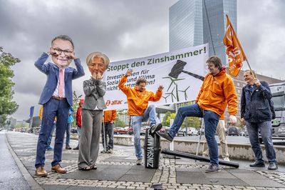 Zwei Attac-Aktivist*innen treten auf den kaputten Zinshammer, Lagarde und Nagel stehen traurig daneben.