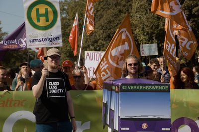 Vor dem Attac-Block laufen zwei Aktivist*innen, einer trägt einen tragbaren Bus, der andere ein Haltestellenschild