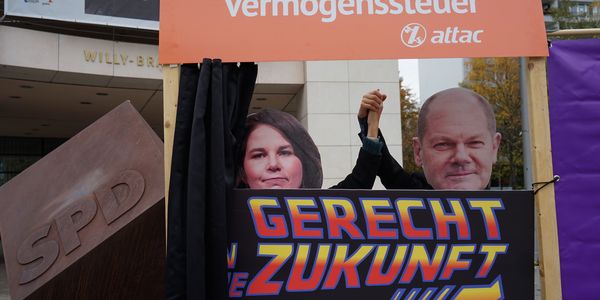 Vor dem Willy-Brandt Haus ist eine Tür mit einem geöffneten Vorhang aufgebaut über dem "Vermögenssteuer" steht, aus der Tür schauen Olaf Scholz und Annalena Baerbock, vor sich ist ein Schild mit dem Slogan "Gerecht in die Zukunft" im Stil des Filmlogos von "Zurück in die Zukunft"