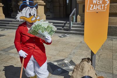 Dagobert steht mit Geldsäcken vor der Börse und wedelt sich mit scheinen Luft zu