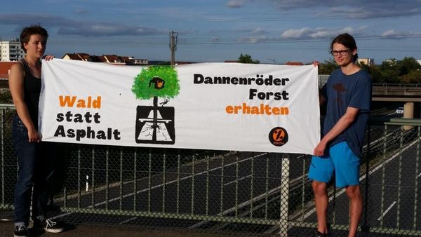 Zwei junge Attacies halten ein Transpi gegen den Bau der A49 und für den Erhalt des Dannenröder Forstes, im Hintergrund ist eine Autobahn