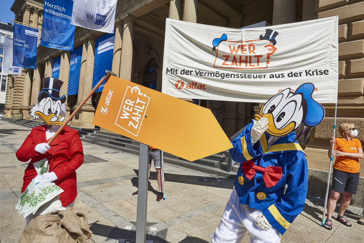 Im Bild sind zwei Aktivist:innen, die als Donald und Dagobert Duck verkleidet sind vor einem Transparent mit der Aufschrift "Wer zahlt? Mit der Vermögensabgabe aus der Krise", Dagobert wedelt mit Geldscheinen und schiebt einen Pfeil auf dem "Wer Zahlt?" steht so, dass er auf Donald zeigt