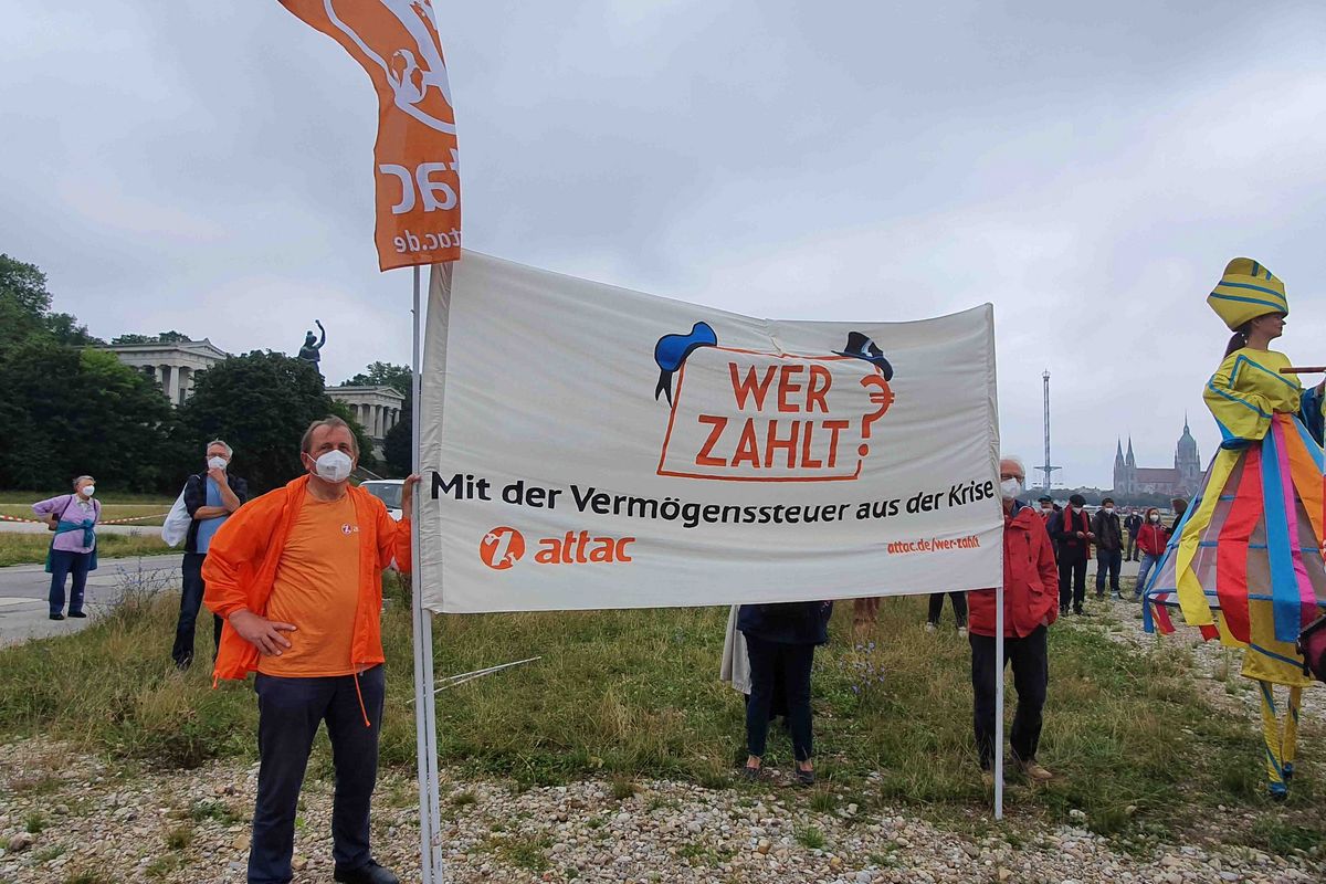 Attacies halten ein Transparent mit dem Slogan "Wer zahlt? Mit der Vermögenssteuer aus der Krise", im Hintergrund weitere Demonstrant*innen