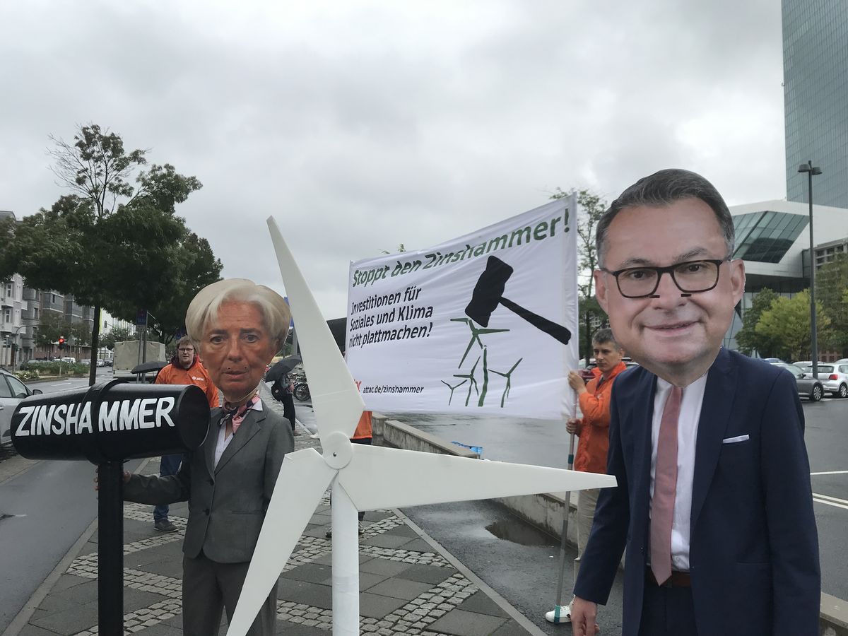 Vor der EZB stehen zwei Aktivist*innen in Anzug und Blazer, die sich als Bundesbankchef Nagel und EZB-Präsidentin Lagarde verkleidet haben, Lagarde hält einen überdimensionierten Hammer, auf dem "Zinshammer steht" im Hintergrund halten Aktivist*innen ein Transparent