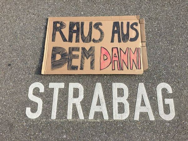 Ein Pappschild liegt auf einem Strabag-Firmenparkplatz, sodass sich die Aussage "Strabag raus aus dem Danni" ergibt
