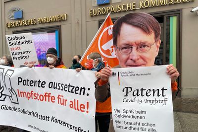 Ein Attacie mit Karl-Lauterbach-Maske hält ein übergroßes Patent auf Corona-Impfstoffe in die Kamera.