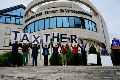 Die Aktivist*innen heben die Buchstaben wie eine La Ole hoch, sodass man "Tax the R" schon liest und die letzten noch die weißen Rückseiten nach vorne halten