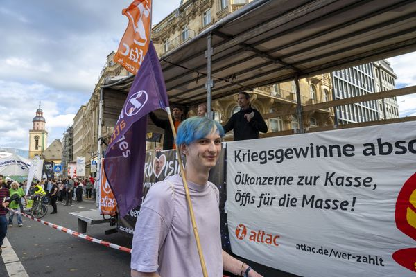 Ein junger Attacke mit blauen Haaren und einer junges-Attac-Fahne läuft neben dem Lautsprecherwagen her, an dem ein Transparent mit dem Slogan "Kriegsgewinne abschöpfen. Ölkonzerne zur Kasse, Öffis für die Masse!" steht