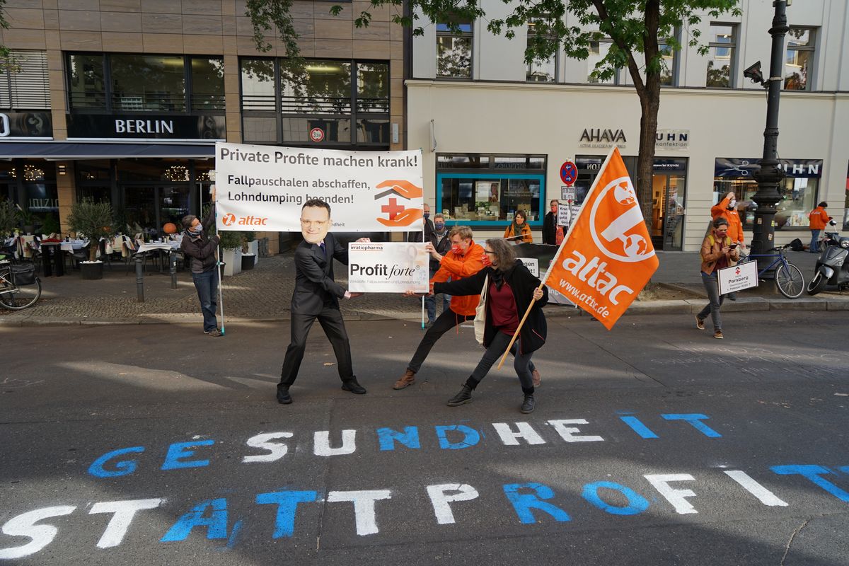 Attacies und ein Mensch mit Jens Spahn Maske Ringen um eine Überdimensionierte Arzeneimittelpackung "Profit forte - Starke Profite auf Kosten Ihrer Gesundheit"