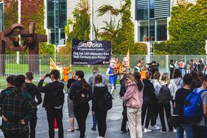 Im Vordergrund ist eine Schulklasse zu sehen, die der Aktion zusehen, im Hintergrund ist die Aktion vor dem Kanzleramt zu sehen.