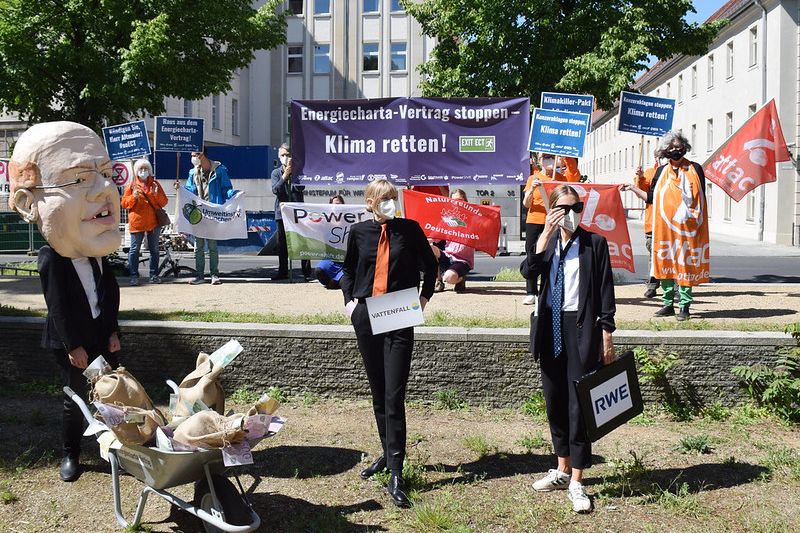 Bild von der Kundgebung, im Vordergrund ein Mensch mit einem Altmaierkopf aus Pappmaché und zwei als Lobbyisten verkleidete Menschen, im Hintergrund Protestierende mit Banner und Fahnen.