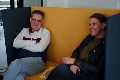 Zwei Menschen sitzen auf einer Bank und lächeln in die Kamera