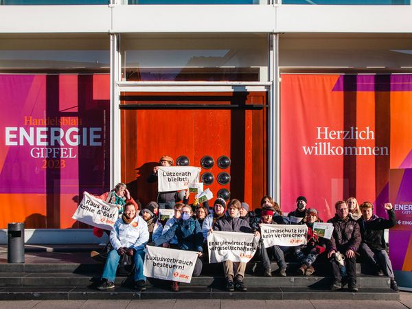 Vor dem Eingang des Handelsblatt-Energiegipfels sitzen ca. zwei Dutzend Aktivist*innen, blockieren den Eingang und halten Banner hoch, die Energiewende fordern.