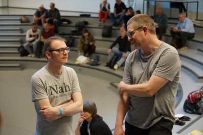 Zwei Menschen unterhalten sich stehend, im Hintergrund ist das Publikum im Plenum zu sehen