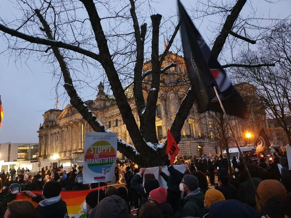 Vor dem Reichstagsgebäude sind im Abendlich viele Demonstrant:innen mit antifaschistischen Transparenten und Fahnen zu sehen. 