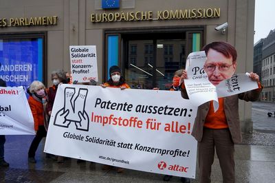 Ein Attacie mit Karl-Lauterbach-Maske zerreißt ein übergroßes Patent auf Corona-Impfstoffe in die Kamera.