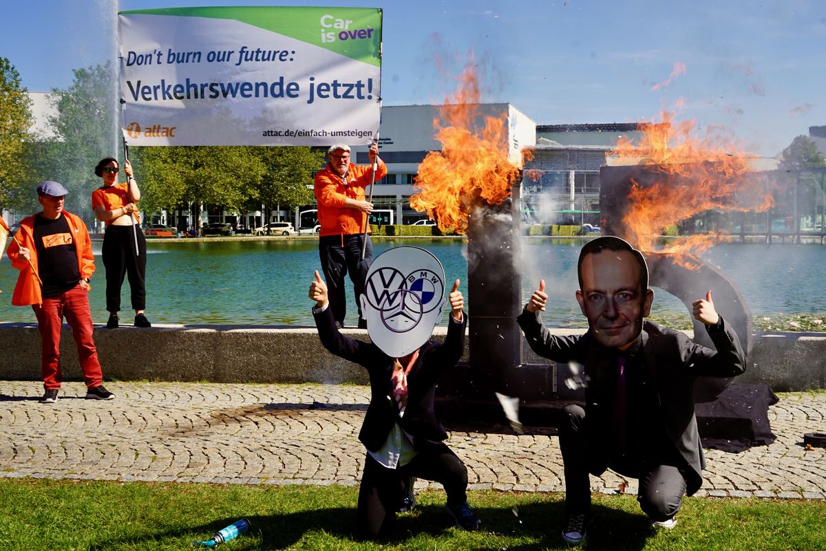 Menschen, die als Wissing und die deutsche Autoindustrie verkleidet sind stehen jubelnd vor einer ca. Menschengroßen 1,5°-Skulptur