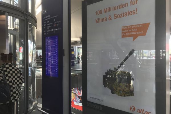 Im Berliner Hauptbahnhof hängt ein geadbustetes Werbeplakat auf dem ein Bus in Tarnfarben mit einem Panzerrohr ist mit einer Sprechblase auf der "Muss ich erst schießen, damit es Geld für den ÖPNV gibt?" steht. Als Überschrift steht "100 Milliarden für Klima und Soziales!" auf dem Plakat